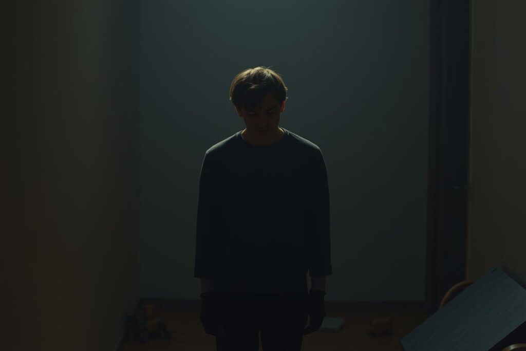 A solitary figure, weighed down by the emotional burdens of parenting, stands in a dimly lit, muted interior. Soft shadows cast on the walls, creating a pensive, introspective atmosphere. The figure's posture conveys fatigue, their expression a mixture of worry and longing. In the background, faint traces of toys and household clutter suggest the demands of family life. The lighting is low-key, with a warm, golden glow illuminating the scene, evoking a sense of melancholy and the need for self-care. A cinematic, almost theatrical composition, capturing the essence of the emotional strain experienced by parents.
